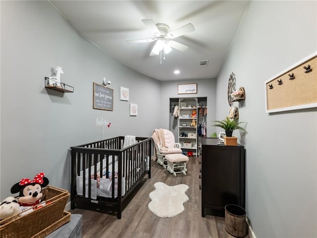 bedroom with ceiling fan, wood-type flooring, and a crib