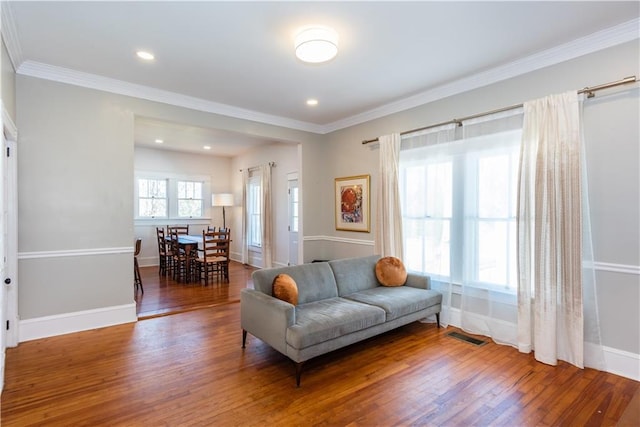 living area with baseboards, visible vents, ornamental molding, and wood finished floors