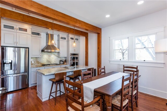 kitchen featuring tasteful backsplash, glass insert cabinets, dark wood-type flooring, stainless steel appliances, and wall chimney range hood