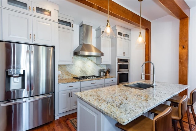 kitchen with a sink, appliances with stainless steel finishes, wall chimney range hood, decorative backsplash, and light stone countertops