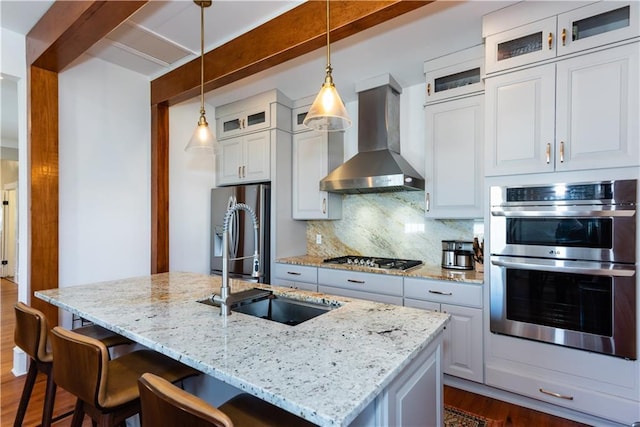 kitchen with decorative backsplash, an island with sink, dark wood-style floors, stainless steel appliances, and wall chimney range hood