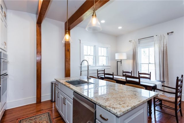 kitchen with appliances with stainless steel finishes, a healthy amount of sunlight, a sink, and beamed ceiling