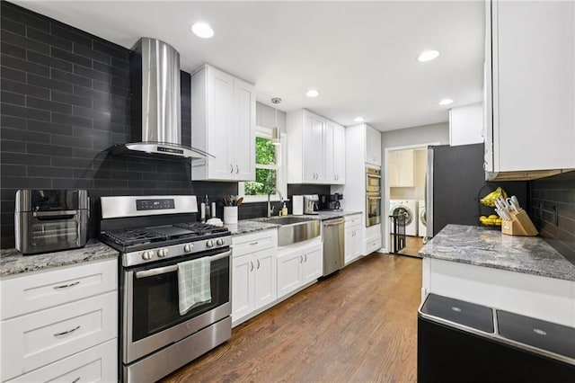 4733 Eidson Rd, Dunwoody, GA 30360 - kitchen featuring appliances with stainless steel finishes, wall chimney range hood, a sink, washing machine and clothes dryer, and dark wood-type flooring