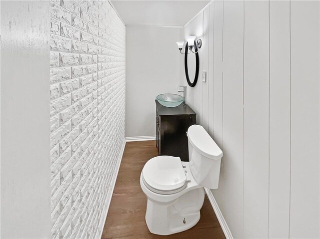 bathroom with vanity, wood-type flooring, toilet, and brick wall