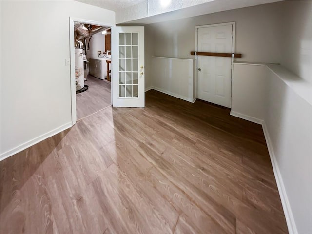 empty room featuring washer / clothes dryer, gas water heater, light hardwood / wood-style floors, and french doors