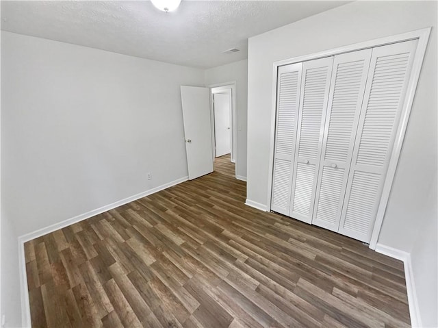 unfurnished bedroom featuring a textured ceiling, dark hardwood / wood-style flooring, and a closet