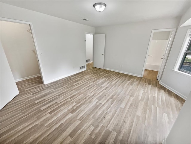 unfurnished bedroom with a closet, a walk in closet, light wood-type flooring, and ensuite bath