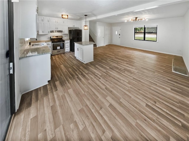 kitchen featuring pendant lighting, white cabinets, a kitchen island, gas range, and black fridge