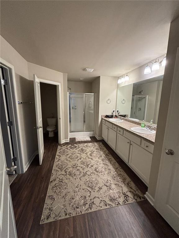 bathroom featuring double vanity, wood finished floors, a sink, and a shower stall