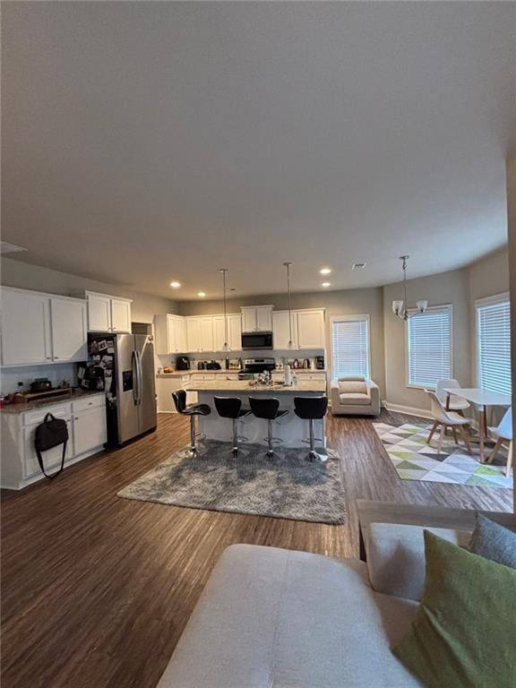 interior space featuring a breakfast bar area, stainless steel appliances, white cabinets, dark wood-style floors, and a center island with sink