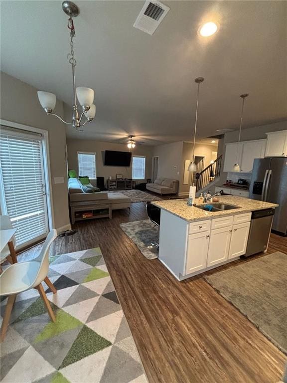 kitchen with stainless steel appliances, a sink, white cabinetry, open floor plan, and a center island with sink