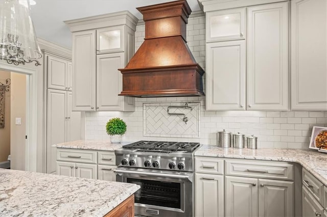 7025 Kettering Ln, Suwanee, GA 30024 - kitchen featuring high end stainless steel range oven, custom exhaust hood, decorative backsplash, glass insert cabinets, and light stone countertops