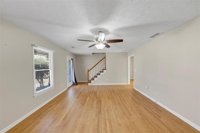 unfurnished room with light wood-style floors, visible vents, baseboards, and stairs