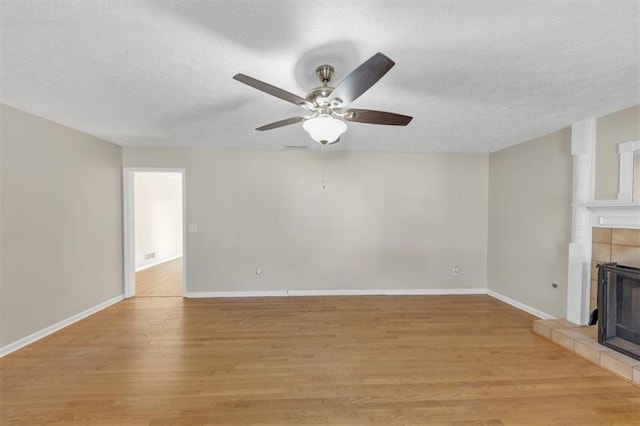 unfurnished living room featuring light wood-style floors, a tile fireplace, a textured ceiling, and baseboards