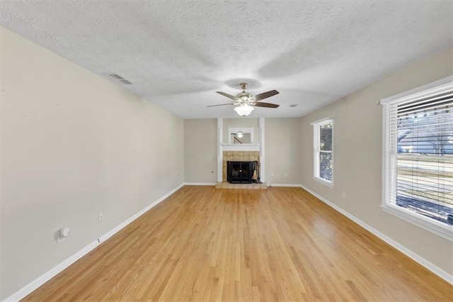 unfurnished living room with a textured ceiling, a fireplace, a ceiling fan, baseboards, and light wood finished floors