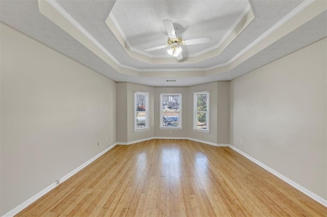 unfurnished room featuring a textured ceiling, wood finished floors, baseboards, ornamental molding, and a raised ceiling