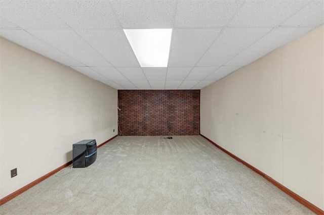 finished below grade area featuring brick wall, a drop ceiling, carpet flooring, and baseboards