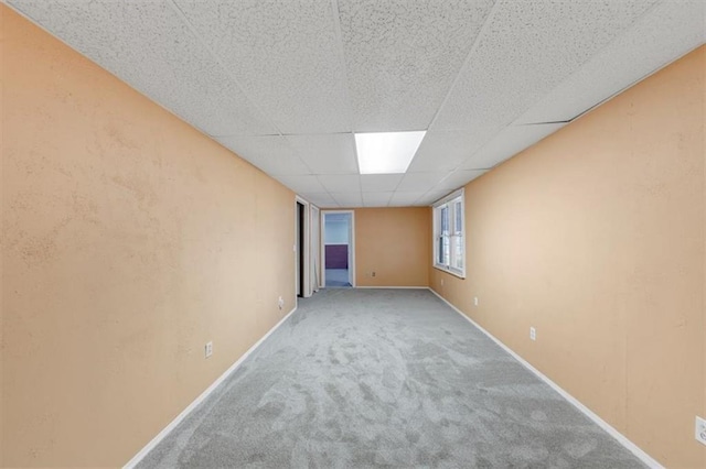 carpeted empty room featuring baseboards and a drop ceiling