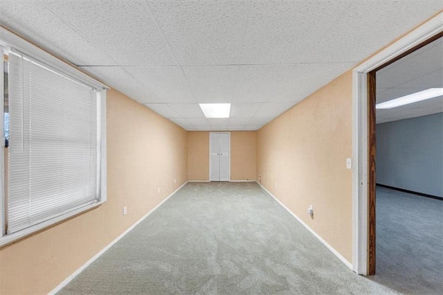 carpeted empty room featuring baseboards and a drop ceiling