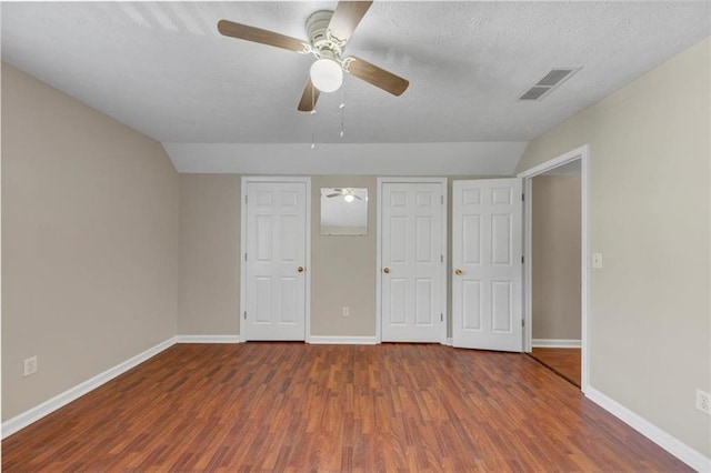 unfurnished bedroom with a textured ceiling, lofted ceiling, wood finished floors, visible vents, and baseboards