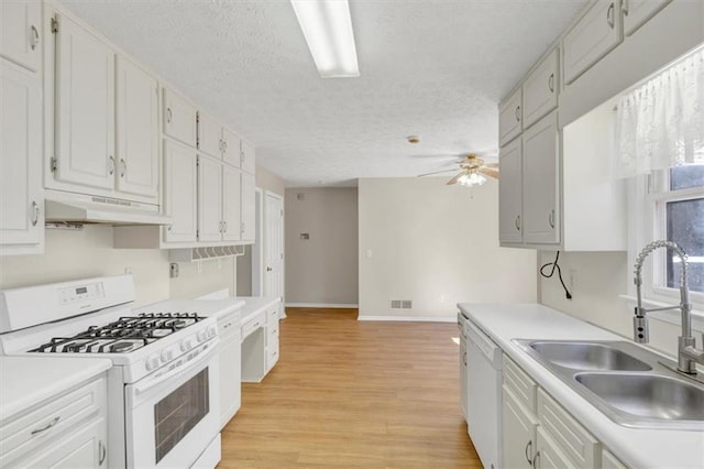 kitchen with white appliances, light wood-style flooring, light countertops, under cabinet range hood, and a sink