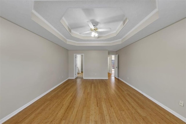 unfurnished room with a tray ceiling, crown molding, ceiling fan, light wood-type flooring, and baseboards