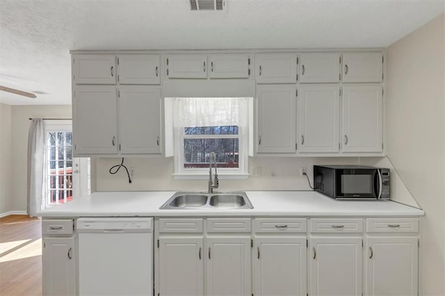 kitchen featuring dishwasher, a sink, black microwave, and white cabinetry