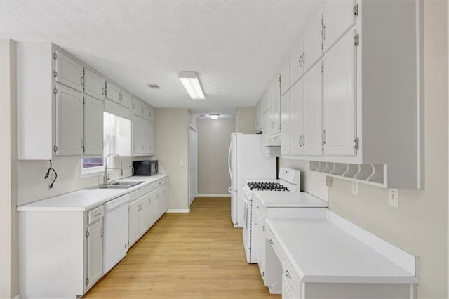 kitchen featuring light countertops, light wood-style flooring, a sink, a textured ceiling, and white appliances