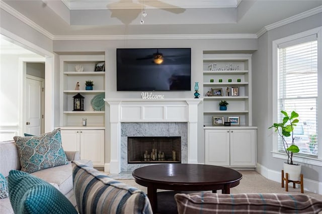 carpeted living room featuring crown molding, a premium fireplace, built in shelves, and a raised ceiling