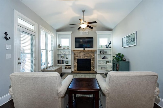 living room with a stone fireplace, vaulted ceiling, built in shelves, and ceiling fan