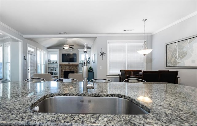 kitchen featuring stone countertops, a fireplace, sink, ceiling fan, and crown molding