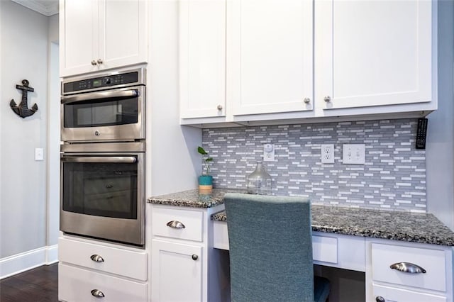 kitchen featuring built in desk, double oven, decorative backsplash, and white cabinets