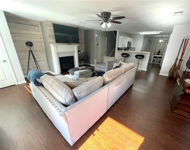 living area featuring baseboards, visible vents, a ceiling fan, dark wood-type flooring, and a fireplace