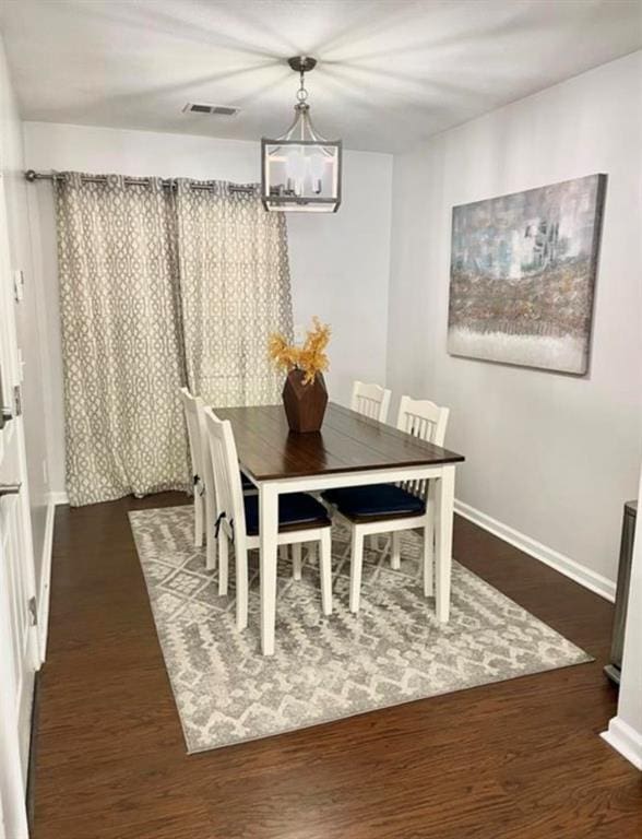 dining room with a notable chandelier, visible vents, baseboards, and wood finished floors