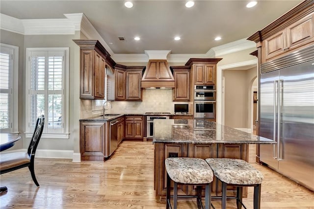 8340 Royal Melbourne Way, Duluth, GA 30097 - kitchen with appliances with stainless steel finishes, premium range hood, ornamental molding, dark stone countertops, and a center island