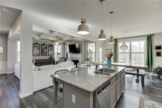 kitchen featuring stainless steel dishwasher, a sink, an island with sink, coffered ceiling, and light stone countertops