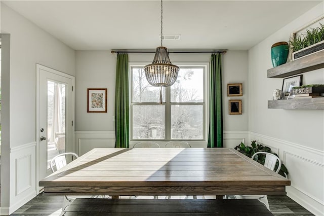 dining area featuring a chandelier, healthy amount of natural light, wood finished floors, wainscoting, and a decorative wall