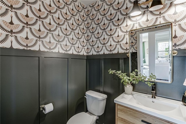 bathroom featuring toilet, vanity, and a decorative wall