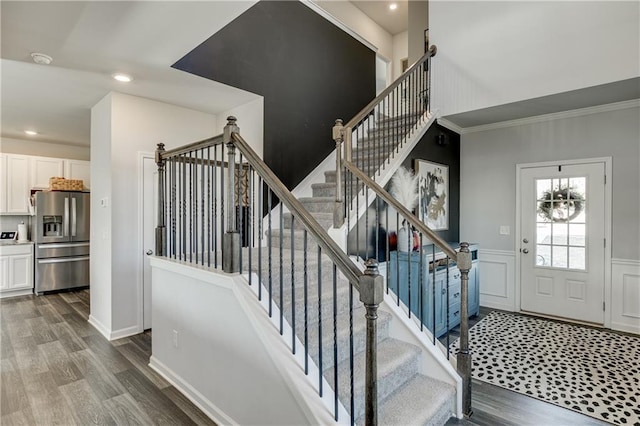 stairway with wood finished floors, recessed lighting, and a wainscoted wall