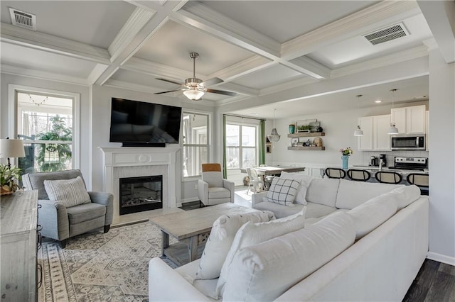 living area featuring coffered ceiling, wood finished floors, a glass covered fireplace, ceiling fan, and beam ceiling