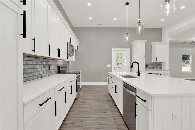 kitchen featuring sink, white cabinetry, hanging light fixtures, stainless steel appliances, and a center island with sink