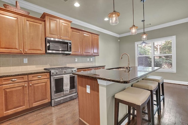 kitchen with an island with sink, stainless steel appliances, dark stone counters, hardwood / wood-style floors, and sink