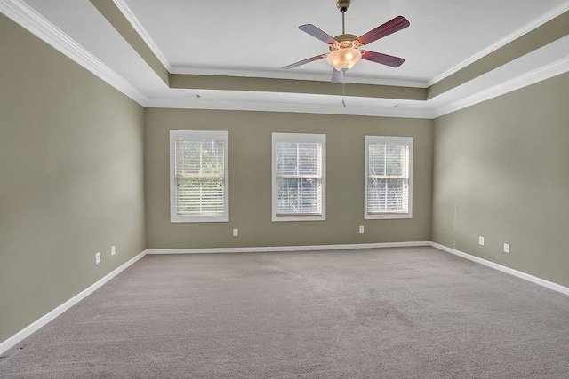 empty room with a raised ceiling, ceiling fan, light colored carpet, and crown molding