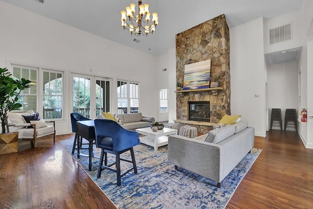 living room with an inviting chandelier, a stone fireplace, dark hardwood / wood-style floors, and a high ceiling