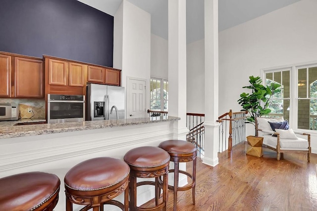 kitchen featuring light stone counters, light hardwood / wood-style flooring, stainless steel appliances, and high vaulted ceiling