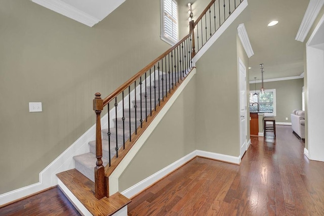 staircase with wood-type flooring and crown molding