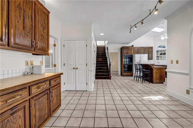 kitchen featuring crown molding, ceiling fan, light tile patterned floors, white fridge with ice dispenser, and dobule oven black