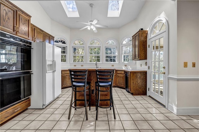 kitchen featuring light countertops, white refrigerator with ice dispenser, light tile patterned flooring, and dobule oven black