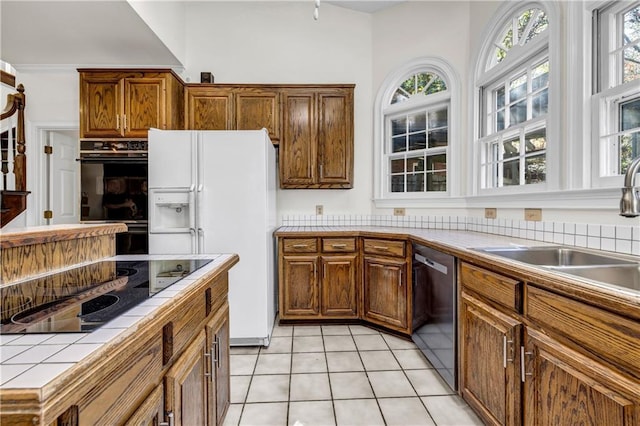 kitchen with light tile patterned floors, a healthy amount of sunlight, a sink, tile counters, and black appliances