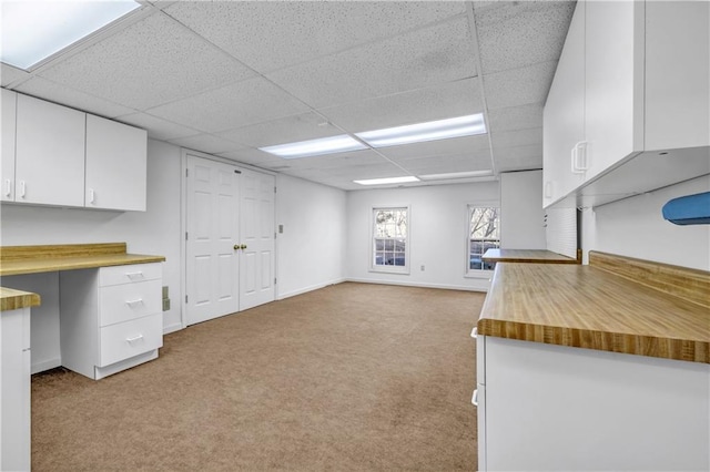 kitchen featuring open floor plan, white cabinets, a paneled ceiling, baseboards, and light colored carpet